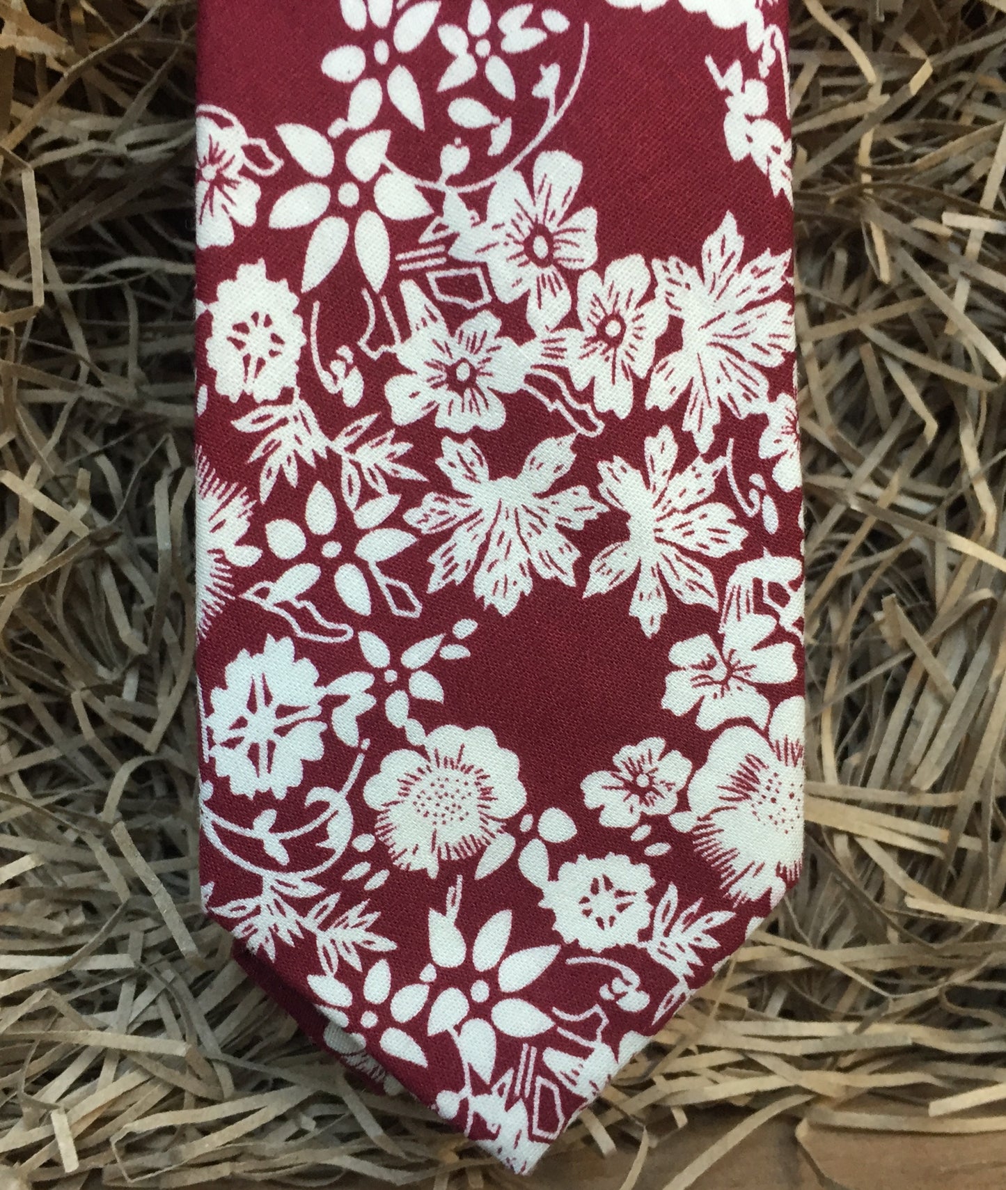 A man's red floral necktie in cotton . This makes a handsome gift for christmas for men or for a groom and his groomsmen. The tie has a red background with white flowers.