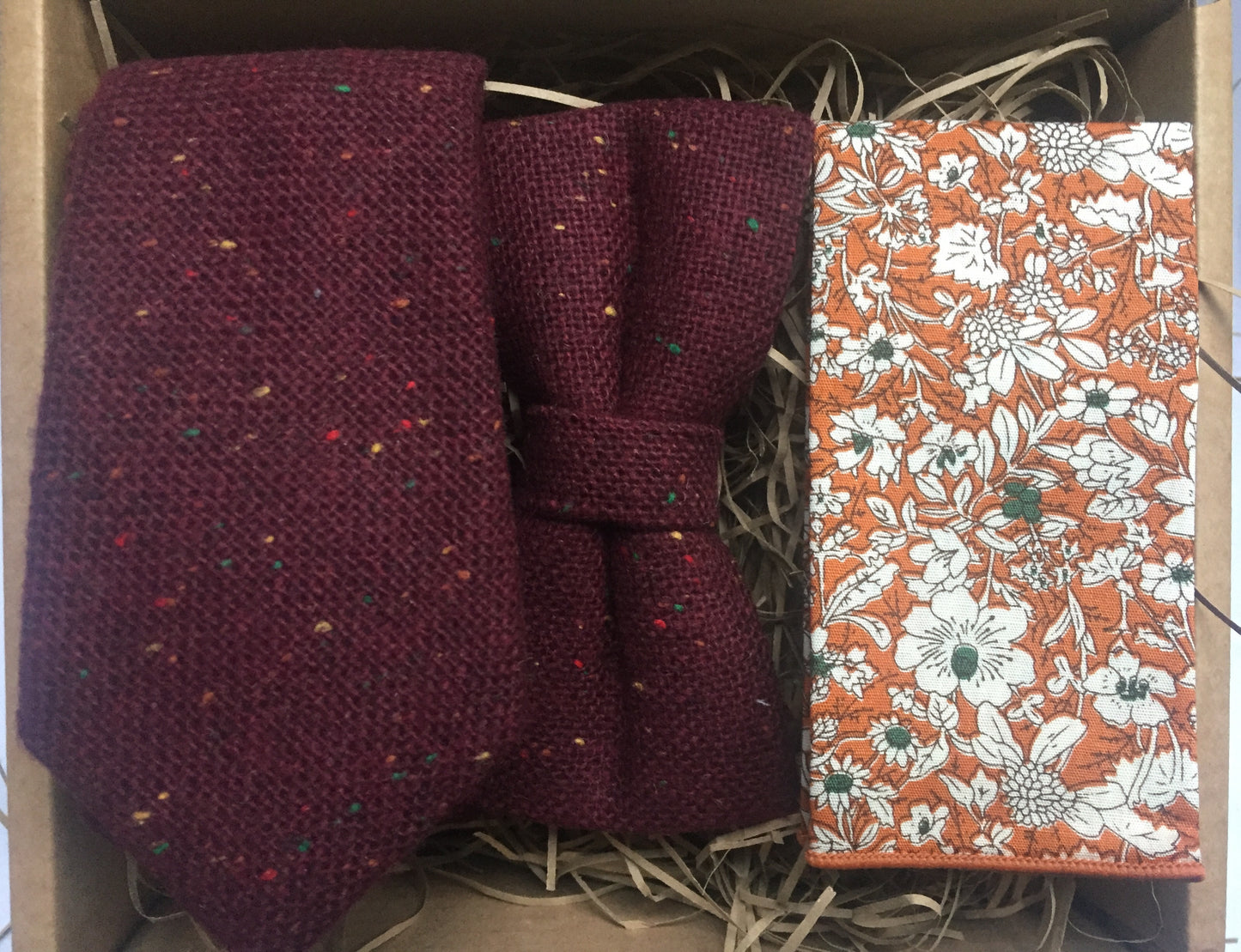 A photo of a men's flecked wool tie, bow tie and pocket square. The fabric is wool and has a red, yellow and green fleck. The ties are handmade by Daisy and Oak Studio and come with beautiful free gift wrapping.