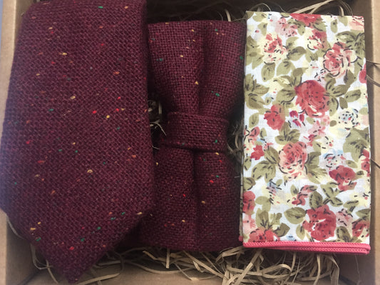 A deep red wool tie, bow tie and pocket square set. The tie is made in wool and is flecked with yellow, red, and blue flecks. The pocket square is a pink floraland handmade at Daisy and Oak Studio, UK