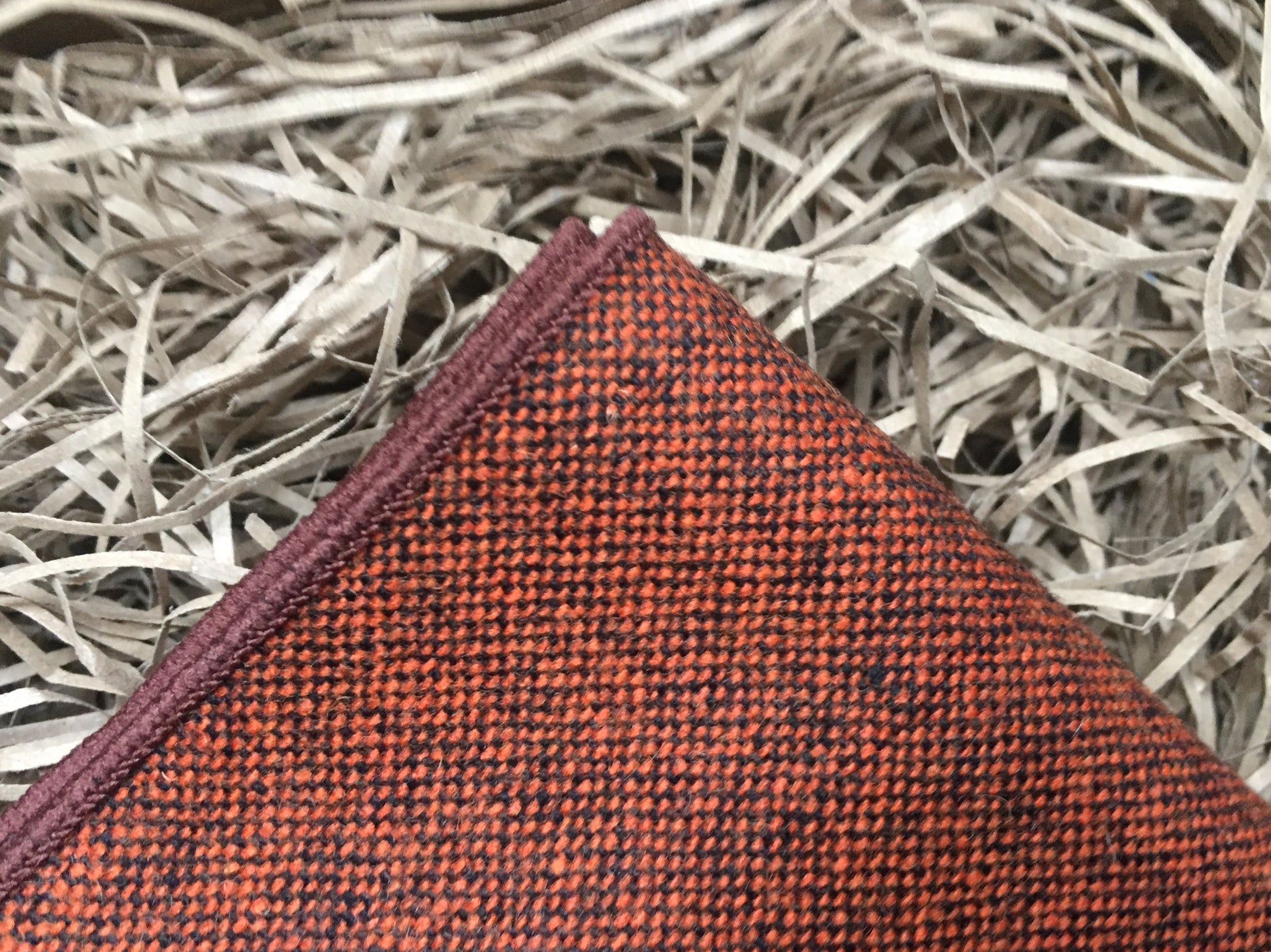 A men's burnt orange wool pocket square worn with a beige checked suit. THe pocket square comes gift wrapped and is handmade by Daisy and Oak Studio.