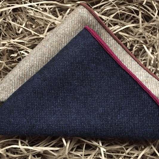 A set of two men's pocket square handkerchiefs in wool. The set has one navy handkerchief with red trim and one beige one. The set is made by hand at Daisy and Oak Studio.